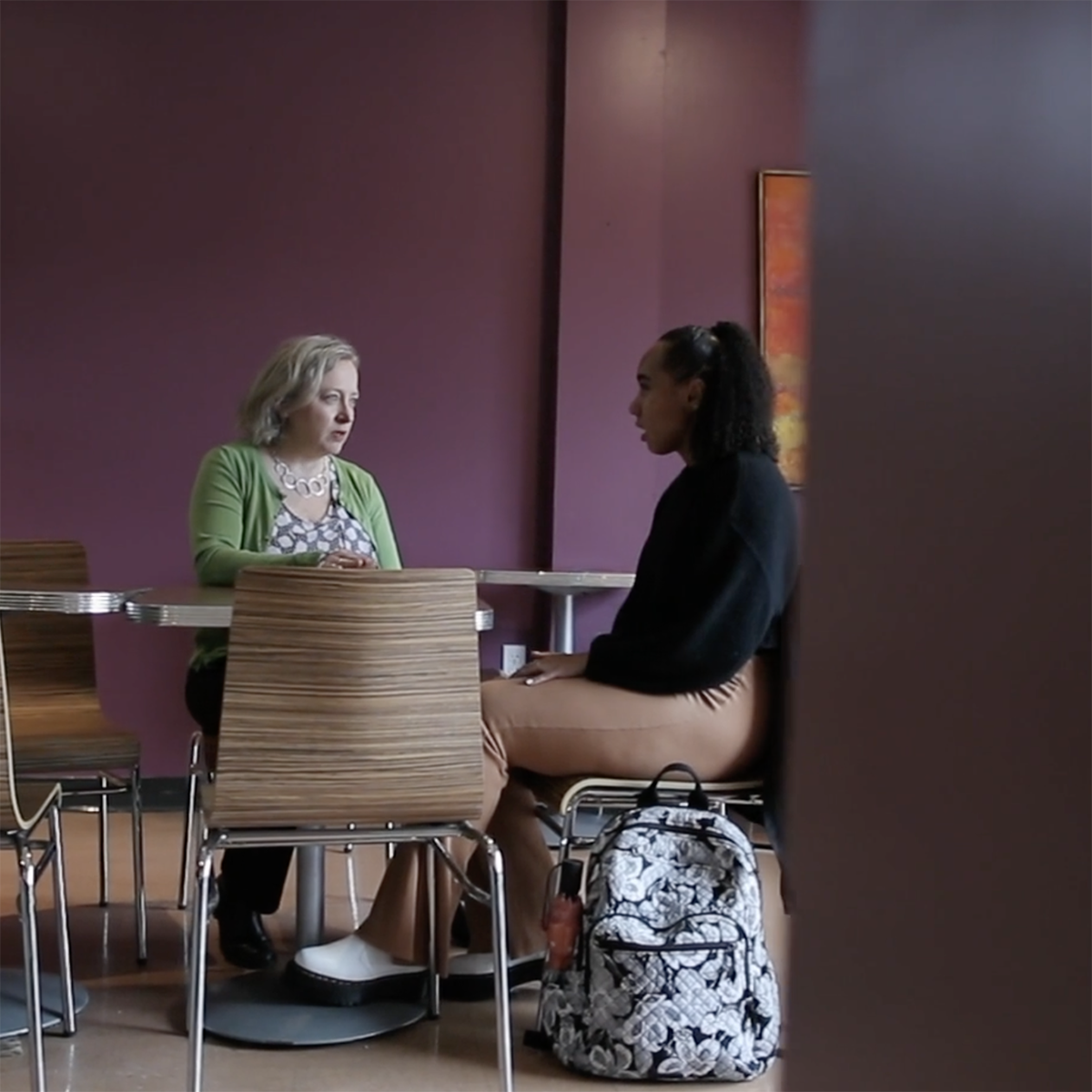 Photo of a faculty member and student seated at a table talking toge的r